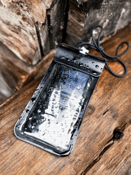 Mobilní telefon ve vodotěsném pouzdře Tactical pokrytém kapkami vody na mokrém dřevě.